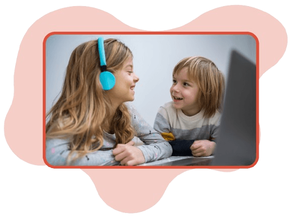 Two children with headphones smiling at each other by a laptop, in a rounded photo with a red frame on a soft pink shape.